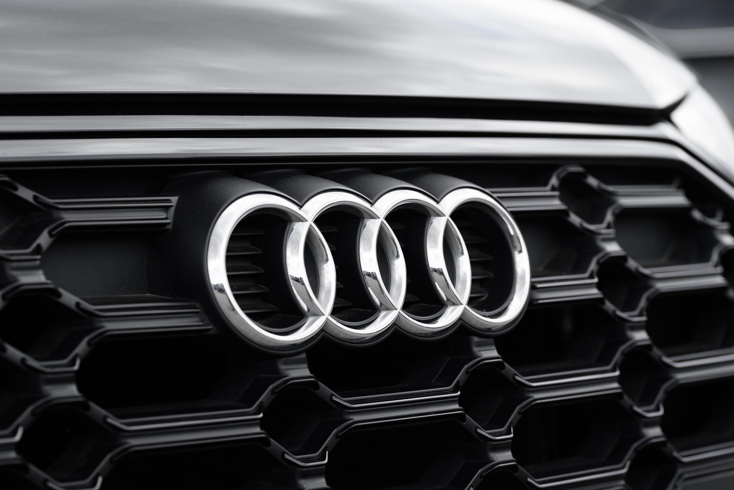 Close-up of the Audi car grille featuring the iconic four-ring logo in silver on a glossy black honeycomb background.