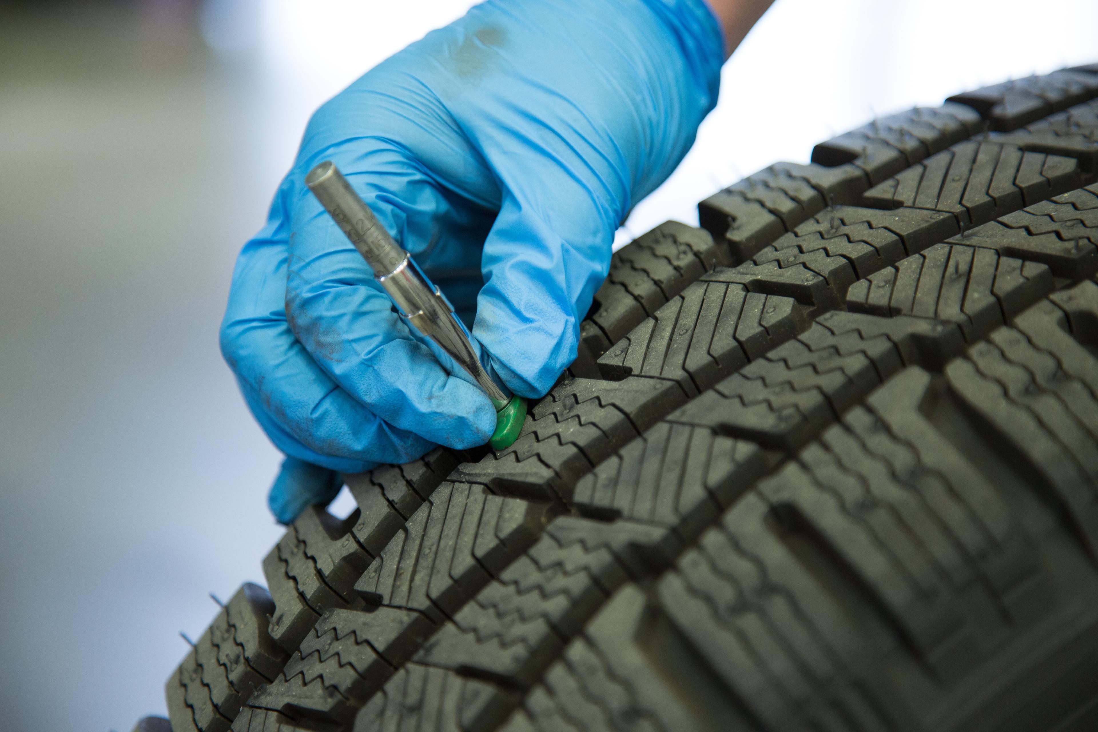 A gloved hand checks tire tread depth using a gauge inserted between the grooves.