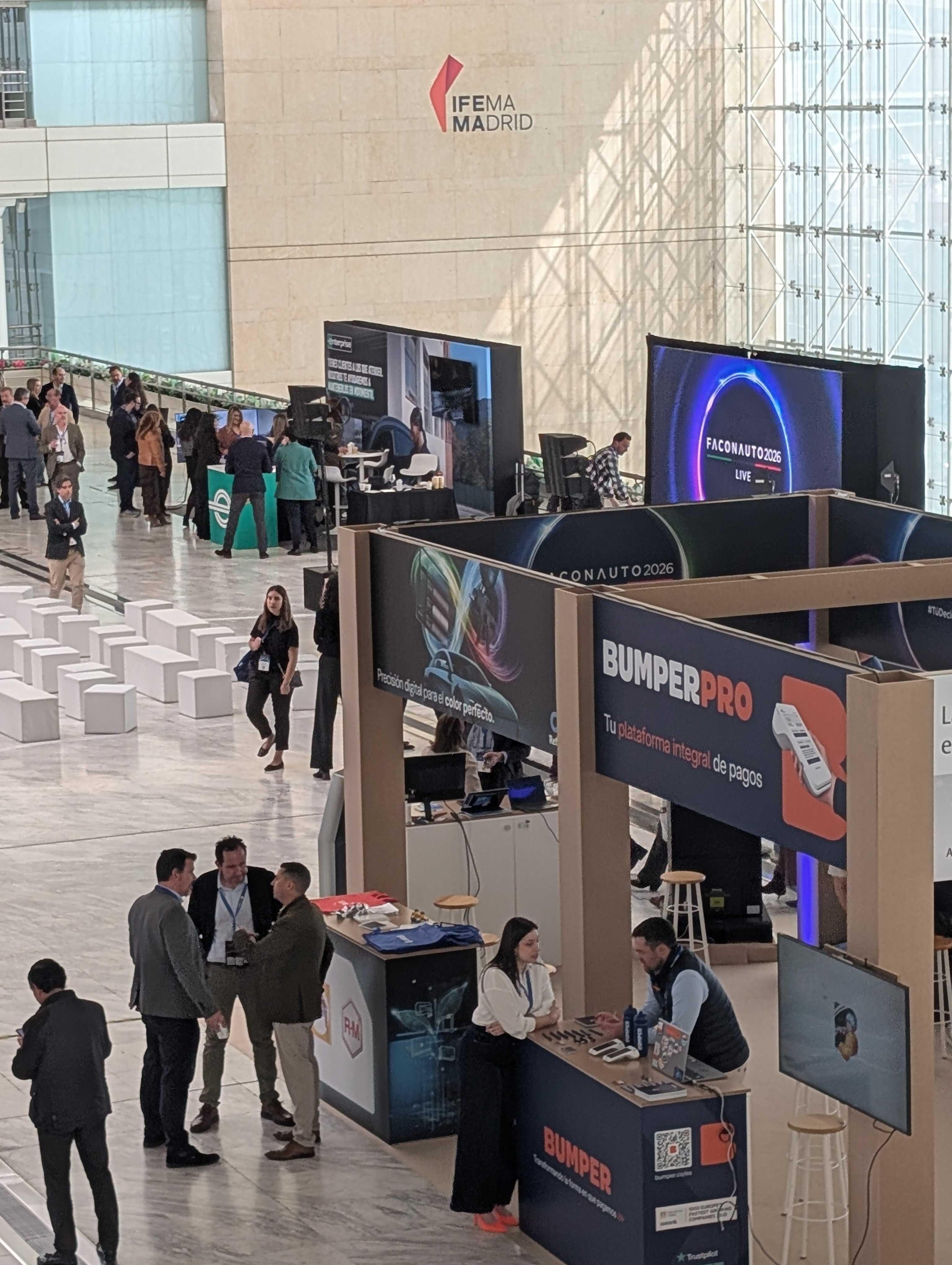 closer-overview-of-faconauto-2026-including-bumper-stand People attending a trade fair at IFEMA Madrid, with various tech booths and displays, including one for BumperPro.