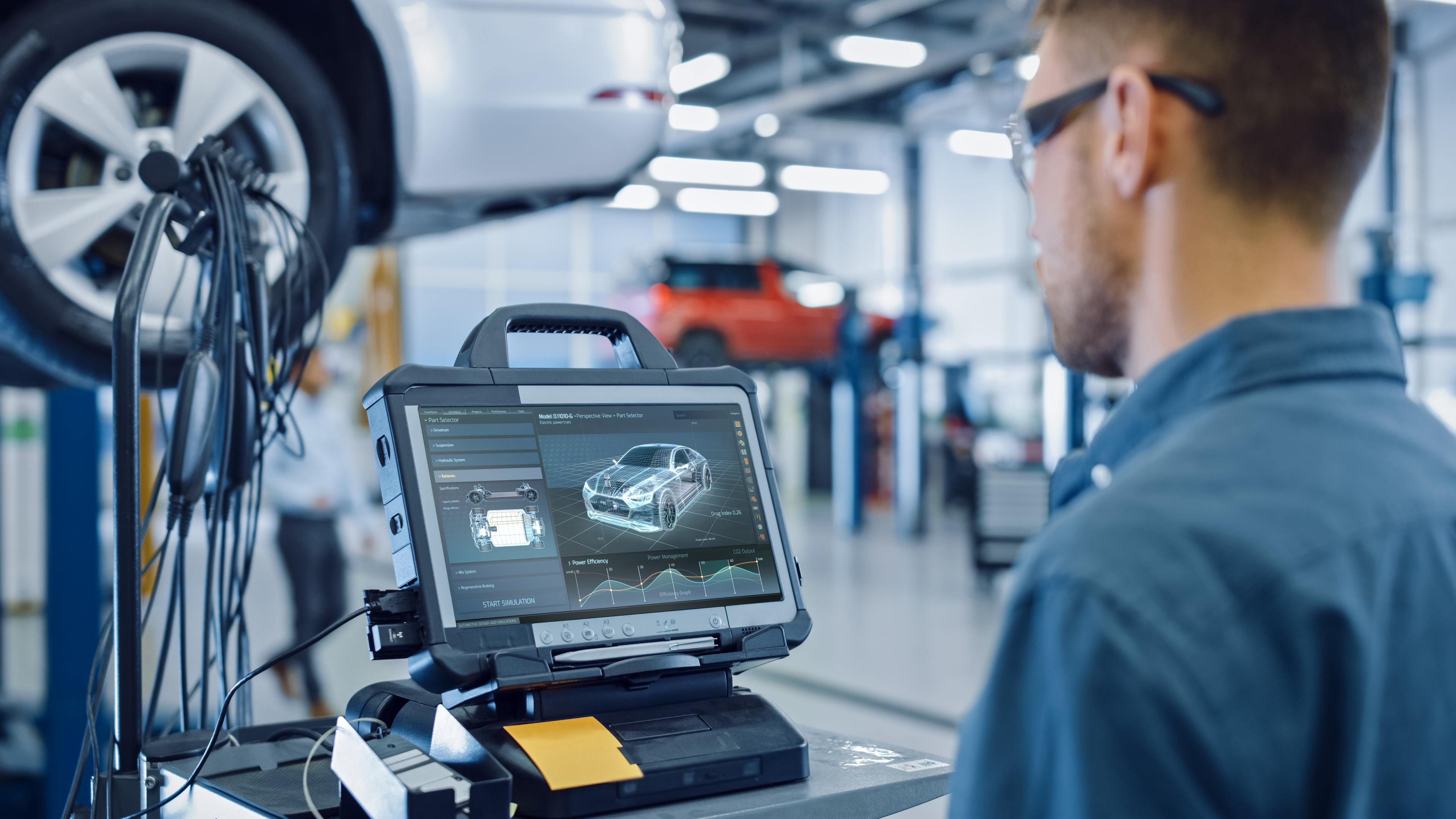 car-technician-checking-digital-data-results Mechanic using diagnostic software on a tablet in a car repair shop, with a vehicle on a lift in the background.